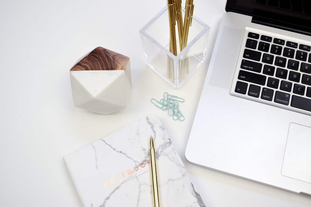 Minimalist white desk with laptop, pens, and notebook.